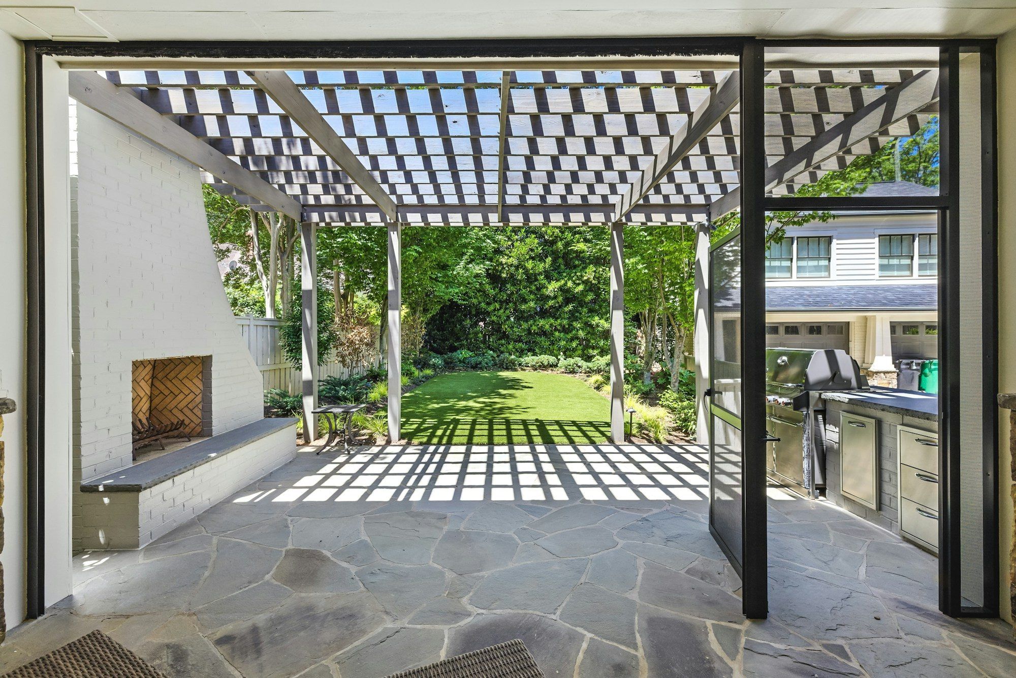 Pergola à lames au-dessus d’une terrasse en pierre, jardin en arrière-plan