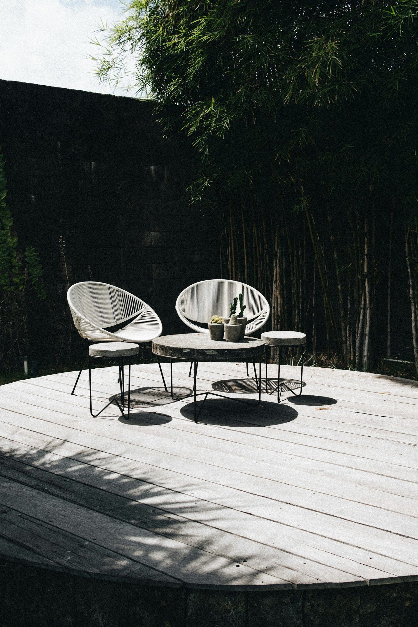 Petite terrasse en bois avec deux fauteuils devant une haie de bambous